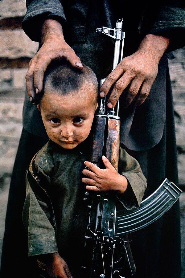 6. Afganistan'ın silâhları çoktan kanıksamış ufaklıklarından birinin arkasında durup onu destekleyen eller