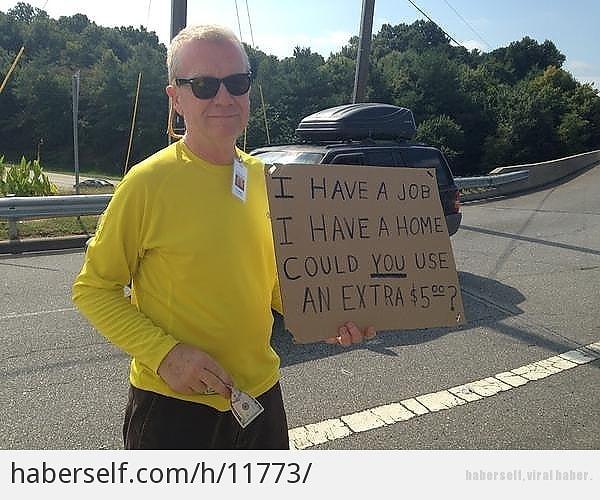 Elinde "İşim var. Evim var. Fazladan 5 dolar ister misiniz?" yazan bir karton taşıyor
