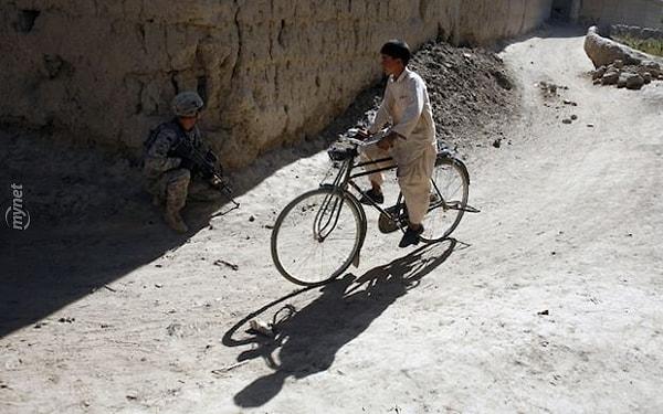 15. Bisikletiyle Amerikan askerinin yanından geçerek okula giden Afgan çocuk. Savaşın ortasından geçerek okula gitmek zorunda kalan milyonlarca çocuktan yalnızca biri... Ahmadanki Köyü, Afganistan.