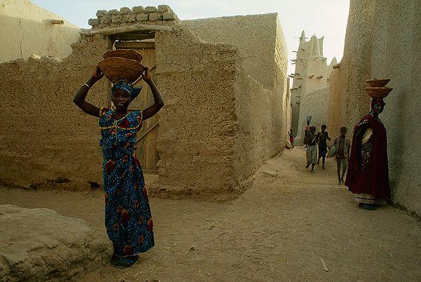 50. Başlarının üzerinde sepet taşıyan kadınlar ve oyun oynayan çocuklar. Kotaka, Mali. 1991.