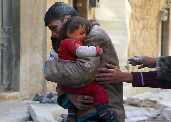 7. Enkaz haline gelmiş evlerinin yıkıntıları arasından kız kardeşini kurtaran Suriyeli bir çocuk.