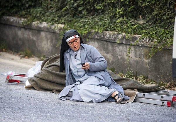 9. Amatrice'de, merdiven üzerine konulan deprem kurbanlarından birinin yanında duran rahibe telefonunu kontrol ederken...