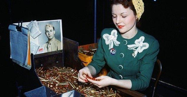 12. Connecticut, ABD. Saldırılarda kullanılacak mermileri tetkik eden bir kadın, Avrupa'da savaşan kocasının fotoğrafının yanında poz verirken.