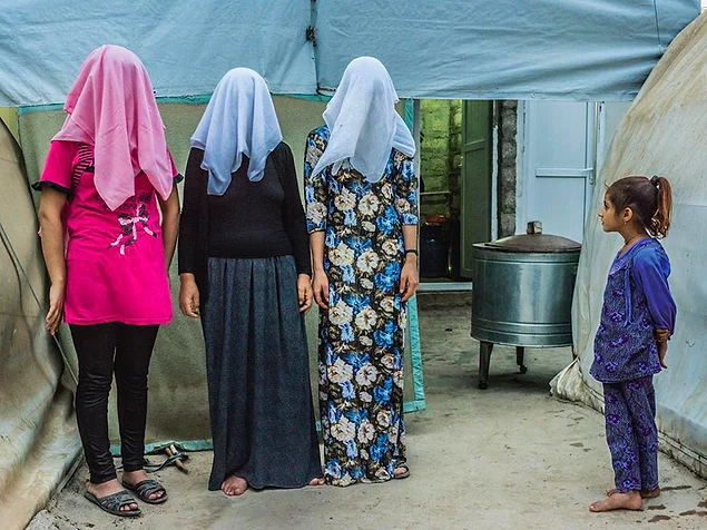 Девочка смотрит, как курдские женщины закрыли свои лица для фото. Две из них признались, что их заставили выйти замуж за бойцов ИГИЛ, но им удалось сбежать