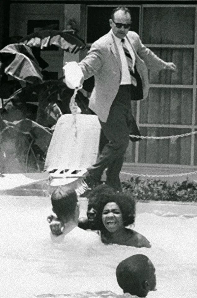 The hotel manager pouring acid in the swimming pool in which swim blacks, 1964. USA.