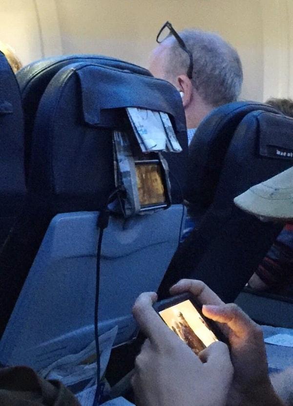 7. Bu dahi arkadaşımızın uçak koltuğuna gazeteyi katlayarak yaptığı telefon tutucu
