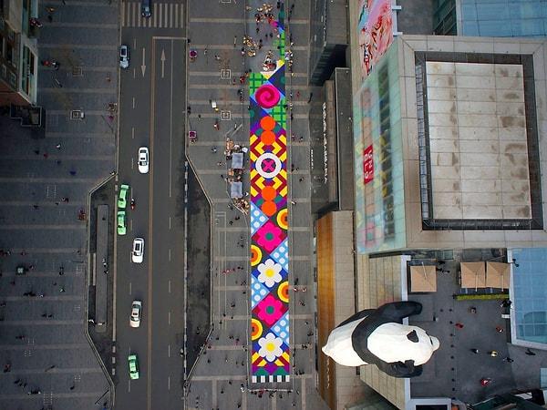 22. İnsanlar Çengdu, Siçuan'da farklı renklerle döşeli 185 metrelik halıyı monte ediyor. Aynı yerde bir de devasa panda heykeli var.
