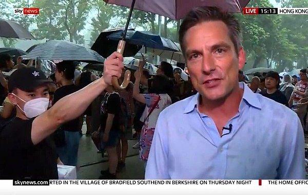 15. Bir gazeteci için şemsiye tutan bir protestocu.