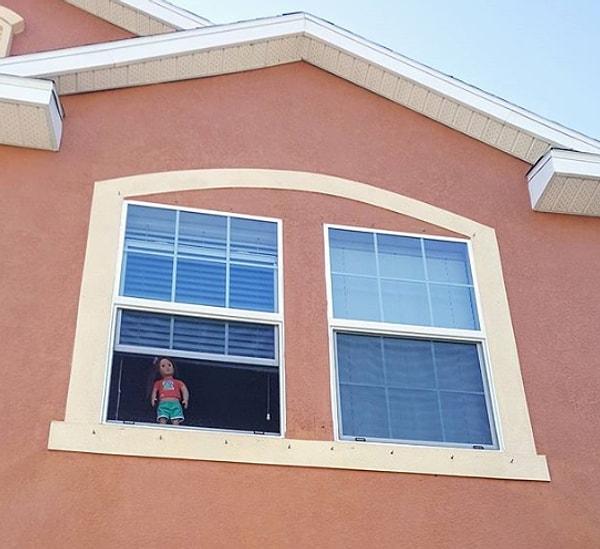 4. Perdesi yarıya kadar çekilmiş pencerenin önüne, oyuncak bebeğini bırakan küçük kız.