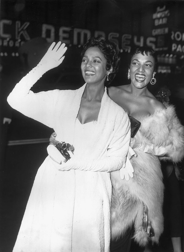 17. Dorothy Dandridge ve kız kardeşi Vivian Dandridge, kırmızı halıda gece elbiseleri ve opera eldivenleri içinde yürüyorlar.