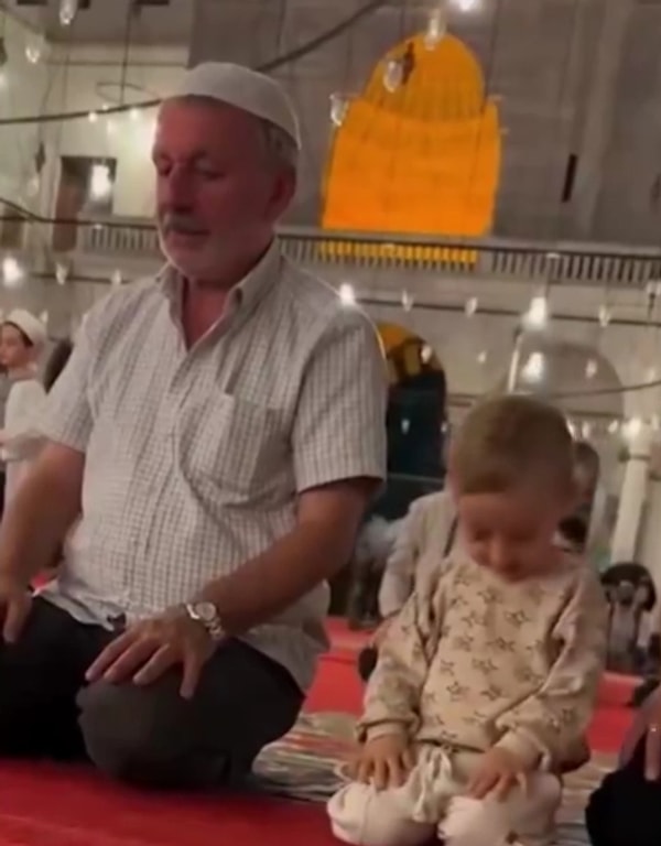 Dedesiyle birlikte camiye giden ufaklık, yanında namaz kılan dedesine eşlik ederken o anlarda Fatiha Suresini okumaya çalışıyor.