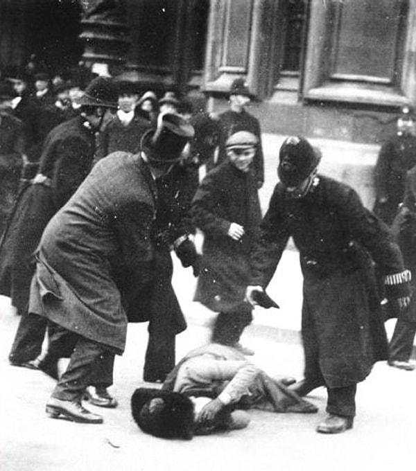 13. Bir adam, 1914'te İngiltere'nin Londra kentinde bir kadın hakları yürüyüşü sırasında bir süfrajeti yere vurduktan sonra polisle boğuşuyor.