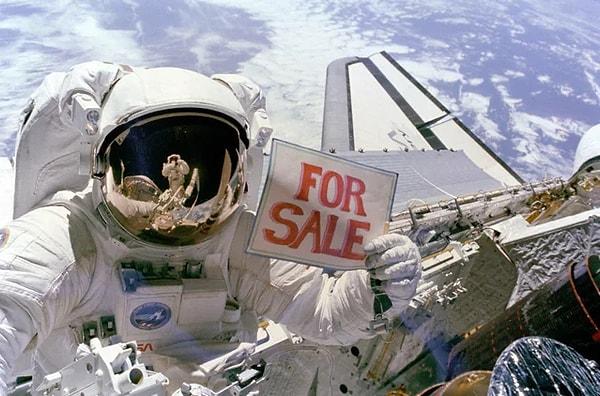 8. Astronot Dale Gardner Uzay Mekiği aracılığıyla Dünya'ya geri gönderilecek olan iki uydunun (sağ altta kısmen görülüyor) elindeki "Satılıktır" tabelasıyla reklamını yaparken. (14 Kasım 1984.)